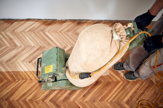Repairman restoring parquet with a sanding machine.