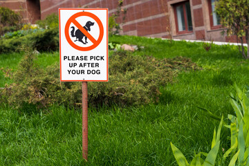 Warning sign: PLEASE PICK UP AFTER YOUR DOG. dog walking is prohibited on the background of the green lawn.