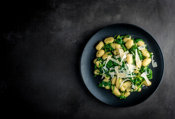 gnocchi with spinach and parmesan on a dark background with copy space