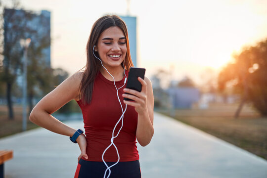 Modern young woman with cellphone making pause during jogging exercise.