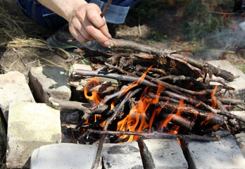 Close-up of a homemade stone grill and a man's hand throwing firewood. Light a fire on the grill