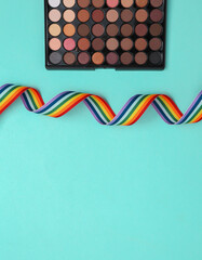 Bright make up eye shadow pallete with rainbow tape on blue background. Beauty still life. Flat lay.