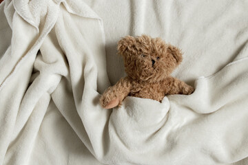teddy brown bear lies in a white blanket on a wooden background close up, soft toy