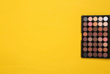 Bright make up eye shadow pallete on yellow background. Beauty still life. Top view. Copy space