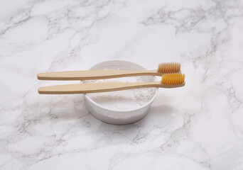 Eco-friendly bamboo toothbrushes and tooth-powder on marble background.