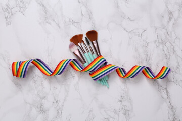 Makeup brushes wrapped in rainbow tape on marble surface. LGBT concept