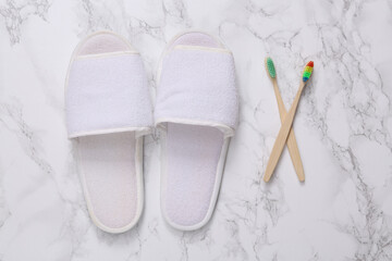 Fototapeta na wymiar White hotel slippers and eco wooden toothbrushes on a marble background.