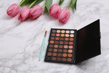 Make-up eye shadow palette with brush and Pink tulips on white marble surface. Romantic, beauty, love concept