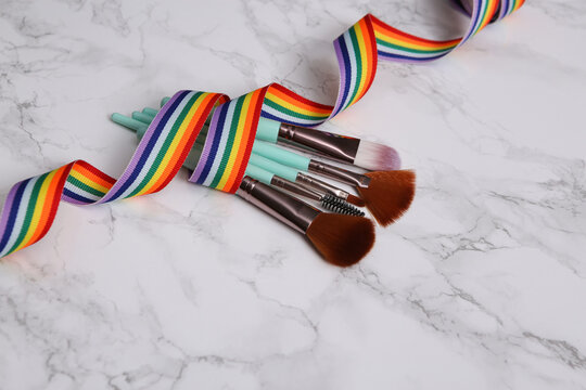 Makeup brushes wrapped in rainbow tape on marble surface. LGBT concept