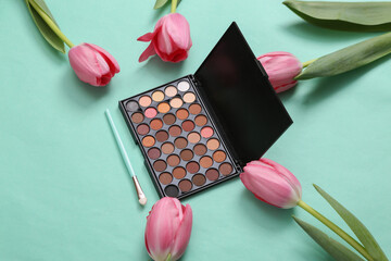 Obraz na płótnie Canvas Make-up eye shadow palette with brush and Pink tulips on blue background. Romantic, beauty, love concept