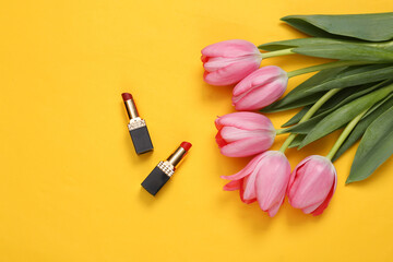 Obraz na płótnie Canvas Lipsticks and pink tulips on yellow background. Romantic, beauty concept