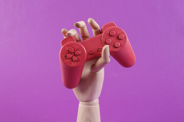 Wooden hand holding gamepad on purple background