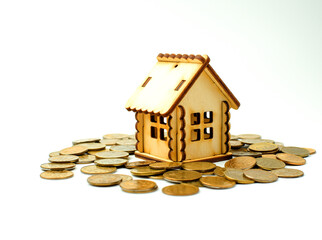 Miniature wooden house stands on top of metal coins, isolated on a white background. Concept of buying and selling apartments, houses. Real estate object. Copy space. Selective focus.
