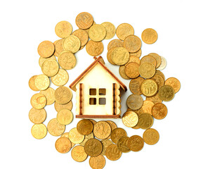 Miniature wooden house lies on metal money, isolated on a white background. Concept of buying, selling and renting residential real estate. Flat lay. Copy space. Selective focus.