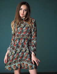 Brunette on a green background stands in a floral dress