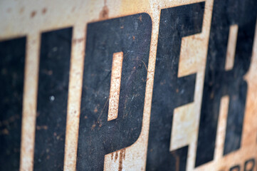 Partial view of an historical advertising sign. Black letters on a metal plate.