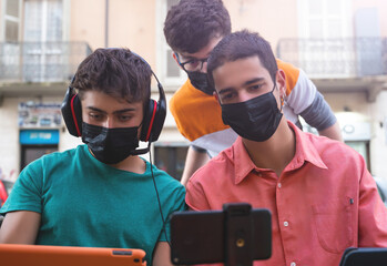 A group of friends is making a live broadcast  from the tables of an outdoor pub. They have masks to defend themselves from the coronavirus. Concept of new normal, friendship and use of technology.