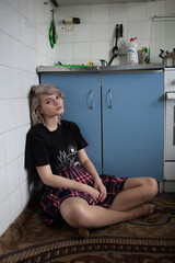 young attractive caucasian female with short hair in black t-shirt and checkered skirt. she is sitting on a floor at old vintage kitchen near a wall with her legs crossed