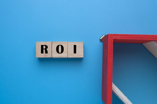 A picture of ROI on wooden block with miniature house roof insight. Return on investment shows how effectively and efficiently investment dollars are used to generate profits.