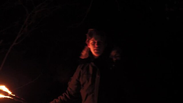 Scared man in night forest fears for an attack waving a torch trying to protect. Suspense atmosphere