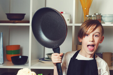 Child at cooking classes. Funny little chef with a pan in kitchen. Boy wearing chef apron.