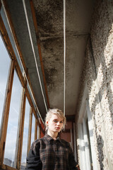 young attractive caucasian female with short hair in checkered shirt standing near window of balcony on sunny day