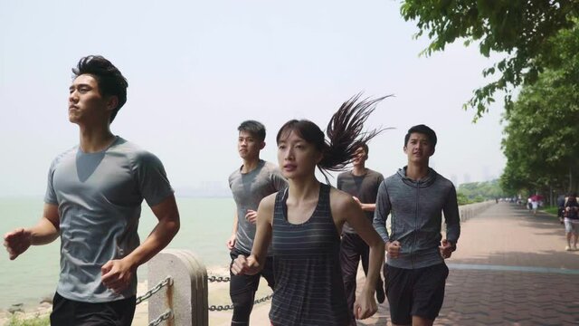 group of five young asian adult men and woman running jogging in seaside park