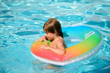 Cute funny little toddler boy relaxing with toy ring floating in a swimming pool having fun during summer vacation in a tropical resort.