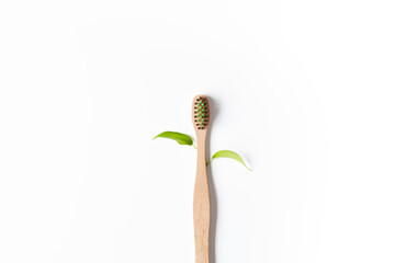 Wooden bamboo dental brush with two green leaves on a white background. Minimalistic composition. Eco-friendly toothbrush, zero waste, copy space.