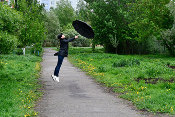 The girl takes off with an umbrella. Strong wind and bad weather. Alley with green trees. 