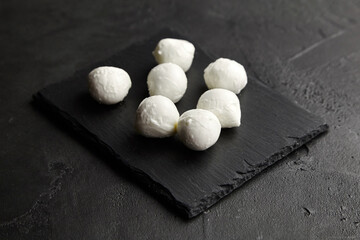 Mozzarella cheese balls on black slate board over dark concrete background