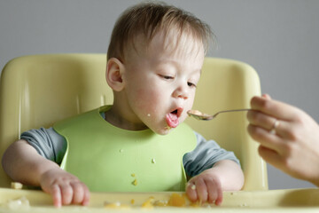 little child eats on gray background, mom feeds the baby with a spoon