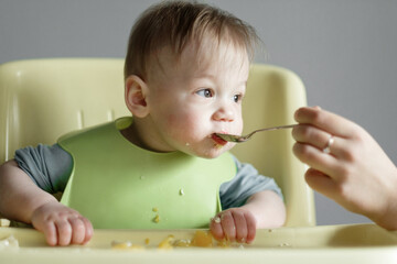 little child eats on gray background, mom feeds the baby with a spoon