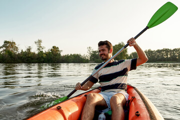 Happy young man smiling while kayaking in a lake, surrounded by peaceful nature on a summer afternoon