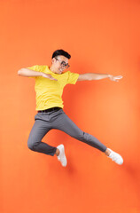 Fototapeta na wymiar Asian man in yellow t-shirt jumping on orange background