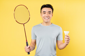 Portrait of an Asian man holding a badminton racket on a yellow background