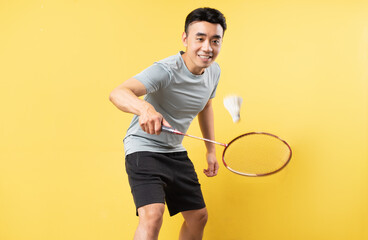 Asian man playing badminton on yellow background