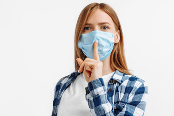 Young woman in a protective mask from viruses, holds the index finger above her lips, makes a gesture of silence, on an white background