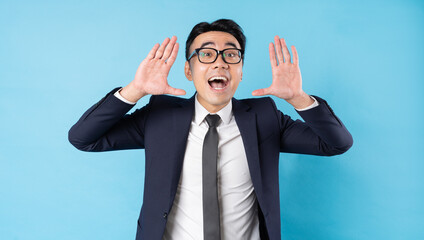 Asian buisnessman wearing suit shouting on blue background