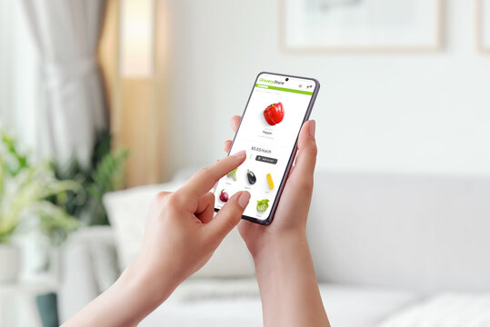 Woman use smart phone for buy groceries. Add red peppers to your shopping cart online concept. Smart phone in woman hands. Home interior in background