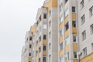 Residential high-rise building with yellow balconies. Against the background of the gray sky. Modern new buildings, building facades. Real estate and urban architecture concept.