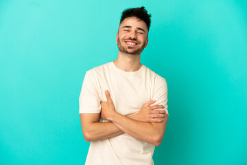 Young caucasian man isolated on blue background keeping the arms crossed in frontal position