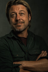 Obraz premium Smiling blond man with stubble beard in green shirt with crossed arms.