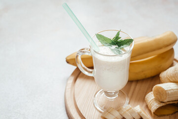 Milk banana shake decorated with mint leaves in a latte glass with handle on light background with...
