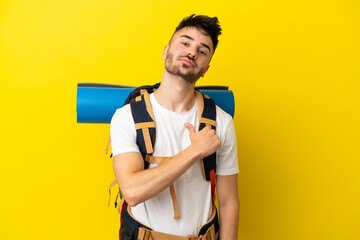 Young mountaineer caucasian man with a big backpack isolated on yellow background proud and self-satisfied