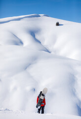 Snowboarder stands against snow mountains and blue sky