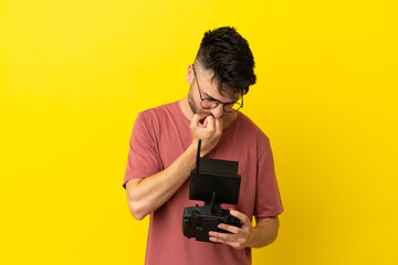 Man holding a drone remote control isolated on yellow background having doubts