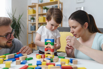 Obraz premium Mother and father playing with their cute smart toddler son at home using colorful wooden toys