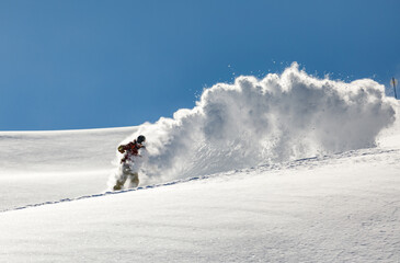 Snowboarder rides on fresh snow in the mountains against blue sky