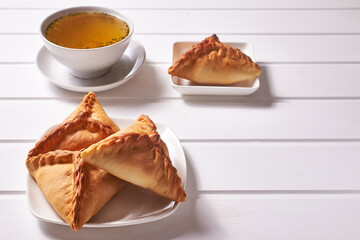 Traditional Tatar pastries "ochpochmak" on a white platter and chicken broth with dill in a white bowl on a white wooden background.